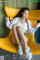 A woman sitting on a yellow chair wearing white sneakers.