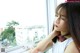 A woman looking out of a window with her hand on her chin.