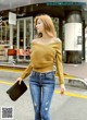 a woman in a yellow sweater and jeans is walking down the street