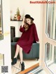 A woman sitting on a couch wearing a burgundy sweater dress.