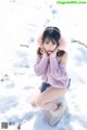 A woman in a pink sweater is sitting in the snow.