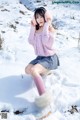 A woman in a pink sweater is sitting in the snow.