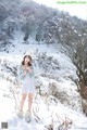 A woman in a white dress and hat standing in the snow.