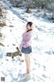 A woman in a pink sweater is standing in the snow.