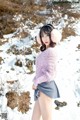 A woman in a pink sweater and gray skirt standing in the snow.