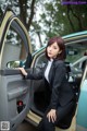 A woman in a business suit sitting in the driver's seat of a car.