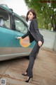 A woman in a business suit leaning against a car.