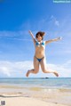 A woman in a blue bikini jumping in the air on a beach.