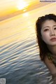 A woman in a bikini standing in the water at sunset.