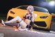 A woman sitting on the ground next to a yellow sports car.