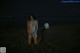 A naked woman kneeling on a beach at night.