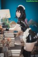 A woman in a maid outfit leaning on a stack of books.