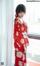 A woman in a red kimono standing by a window.