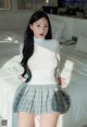 A woman in a white top and plaid skirt posing on a bed.