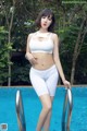 A woman in a white bikini standing next to a swimming pool.