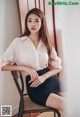 A woman sitting on a chair wearing a white shirt and black skirt.