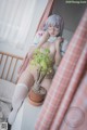 A woman sitting on a bed next to a potted plant.