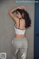 A woman in a white top and gray sweatpants leaning against a wall.