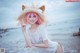 A woman with pink hair wearing a straw hat on the beach.