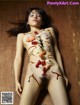 A naked woman laying on a wooden floor covered in sushi.