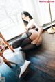 A woman in black stockings and white shoes sitting on a wooden floor.