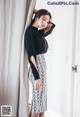 A woman leaning against a curtain in a black top and snakeskin skirt.