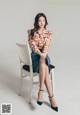 A woman sitting on a chair wearing a floral shirt and skirt.