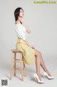 A woman sitting on a stool wearing a white top and yellow skirt.