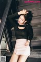 A woman in a black top and pink skirt sitting on some stairs.