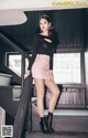 A woman in a black top and pink skirt posing on a staircase.