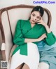 A woman in a green blouse and white skirt sitting on a chair.