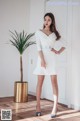 A woman in a white dress standing next to a plant.