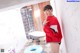 A woman in a red sweatshirt and black shorts posing in a bathroom.