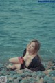 A woman sitting on a rocky beach next to the ocean.