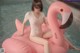 A woman sitting on an inflatable flamingo in a pool.