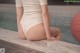 A woman in a white bodysuit sitting on the edge of a pool.