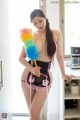 A woman in lingerie holding a colorful duster in a kitchen.